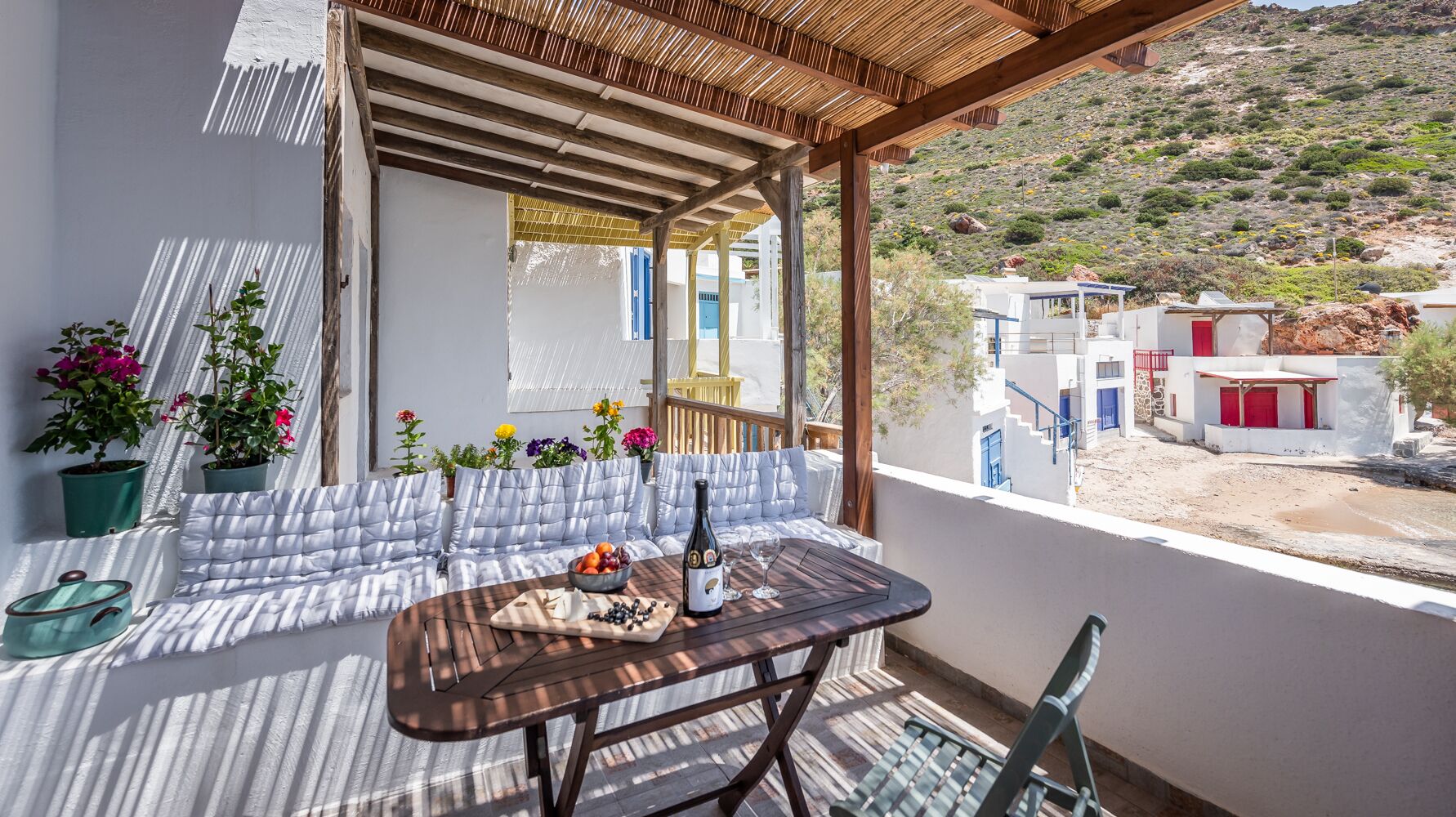 Un balcon avec une table en bois dressée pour les repas, un coin salon avec des coussins et des plantes en pot.