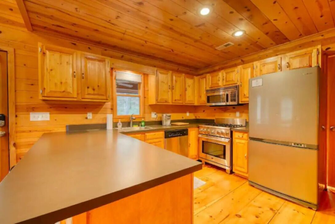 A wooden cabin interior with a kitchen featuring wooden cabinets, a stainless steel refrigerator, a microwave, an oven, and a dishwasher.