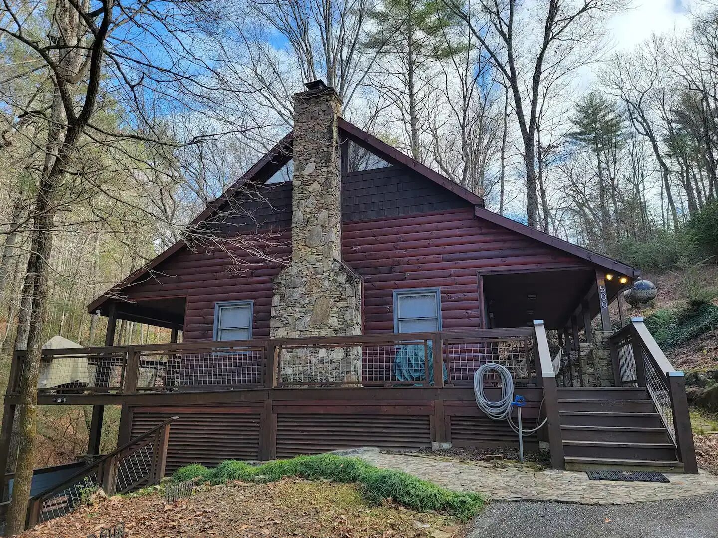 A log cabin with a stone chimney, a covered porch, and a staircase leading to the entrance.