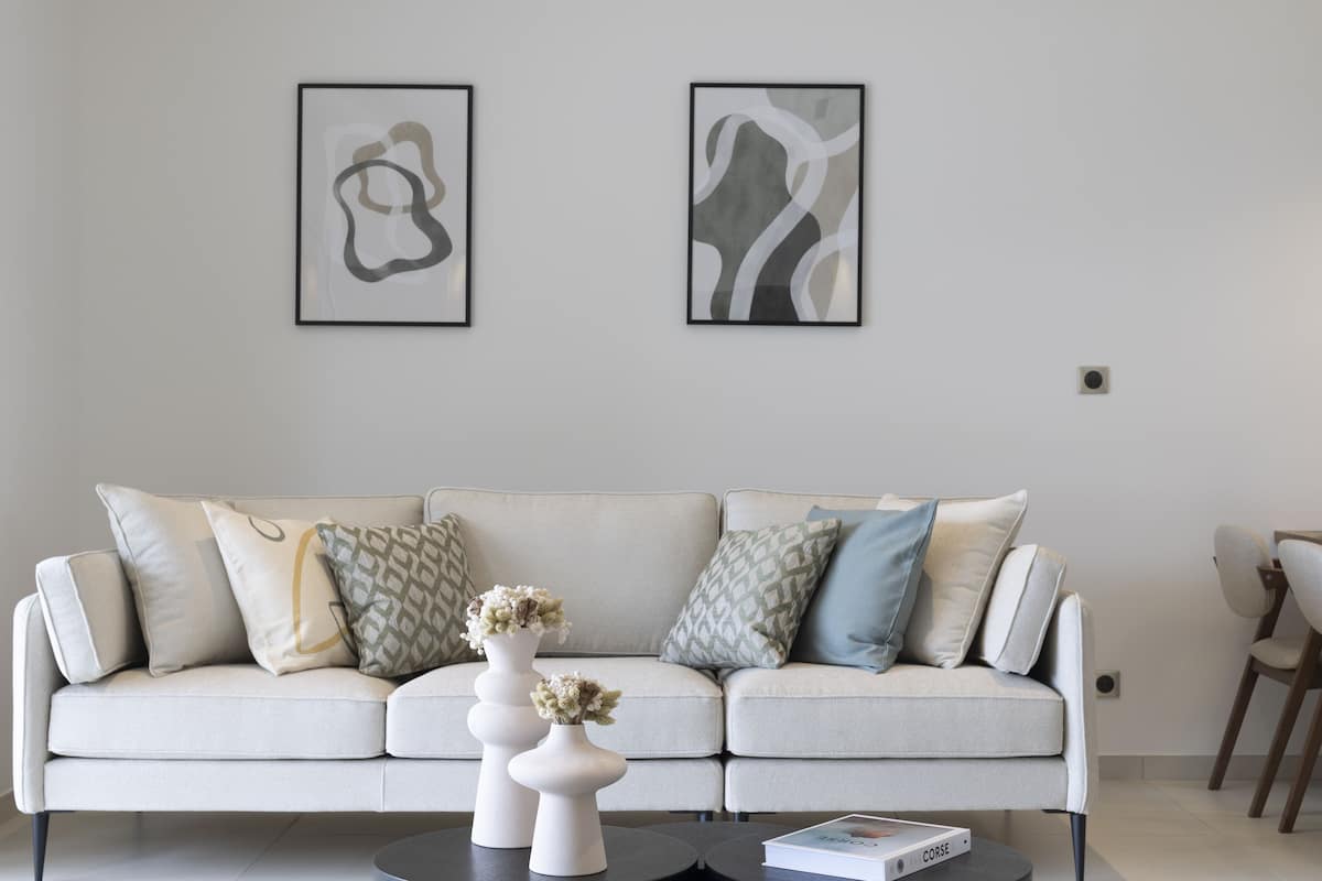 A modern living room with a sofa, two vases with flowers, and abstract art on the wall.
