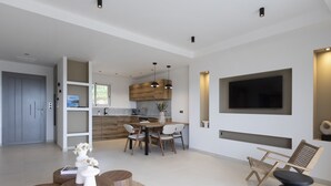 Una sala de estar moderna con comedor, televisor montado en la pared y cocina al fondo.