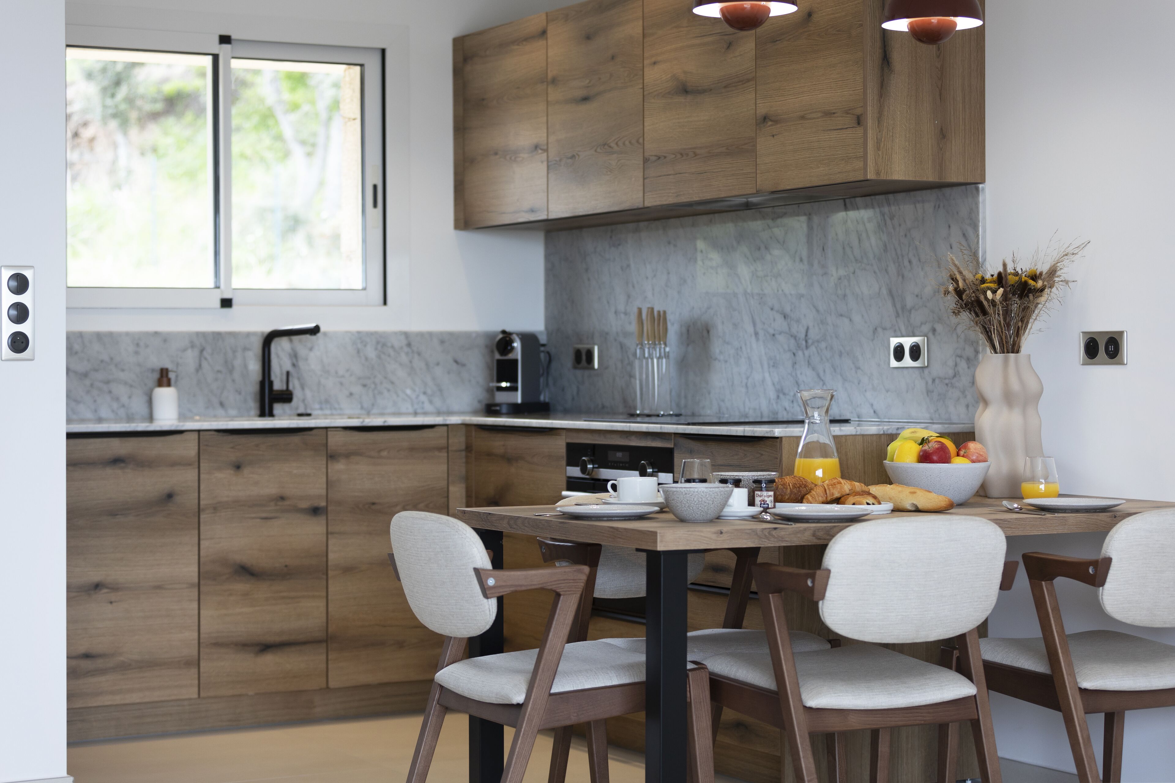Una cocina moderna con armarios de madera, un salpicadero de mármol y un comedor con sillas y una mesa lista para el desayuno.