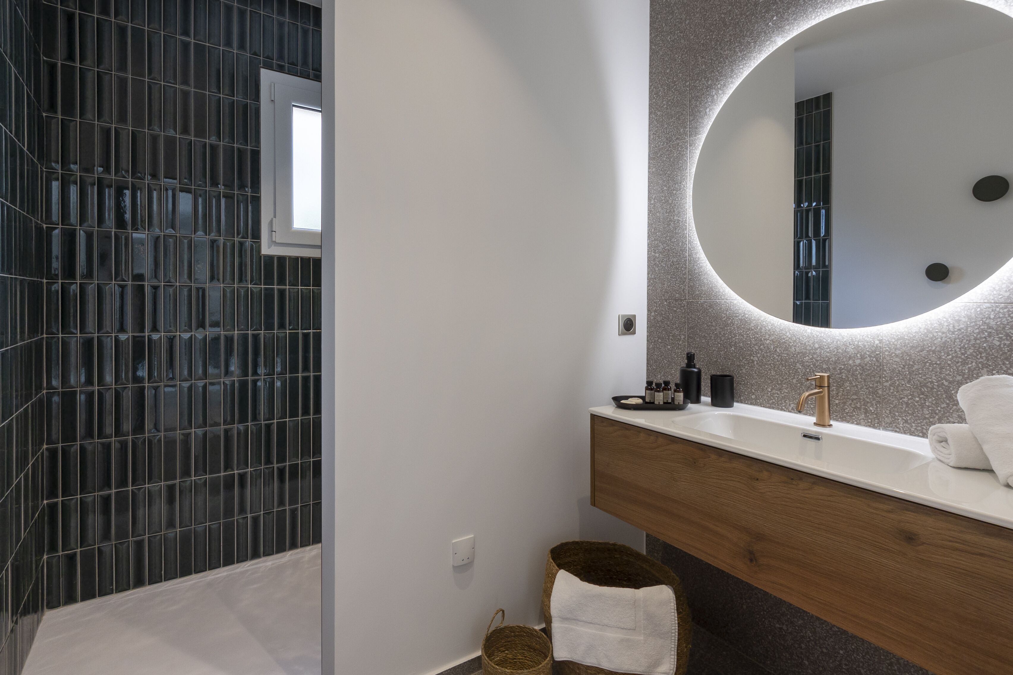 Un baño moderno con un espejo grande, un tocador de madera y una zona de ducha con azulejos.