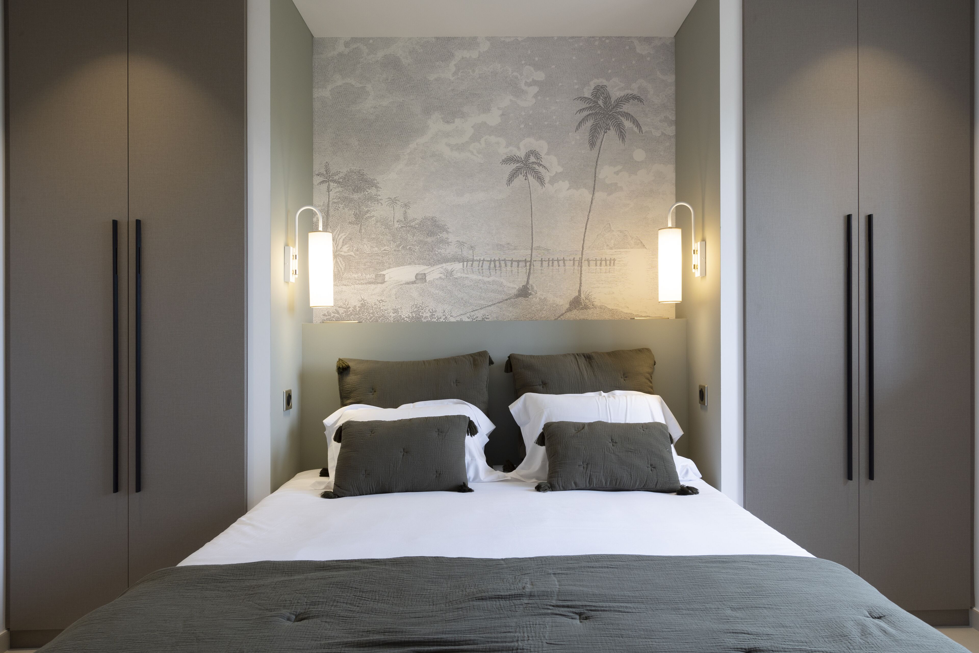Un dormitorio con una cama, dos mesitas de noche, una lámpara de pared y un mural con una escena de playa.