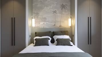 Un dormitorio con una cama, dos mesitas de noche, una lámpara de pared y un mural con una escena de playa.