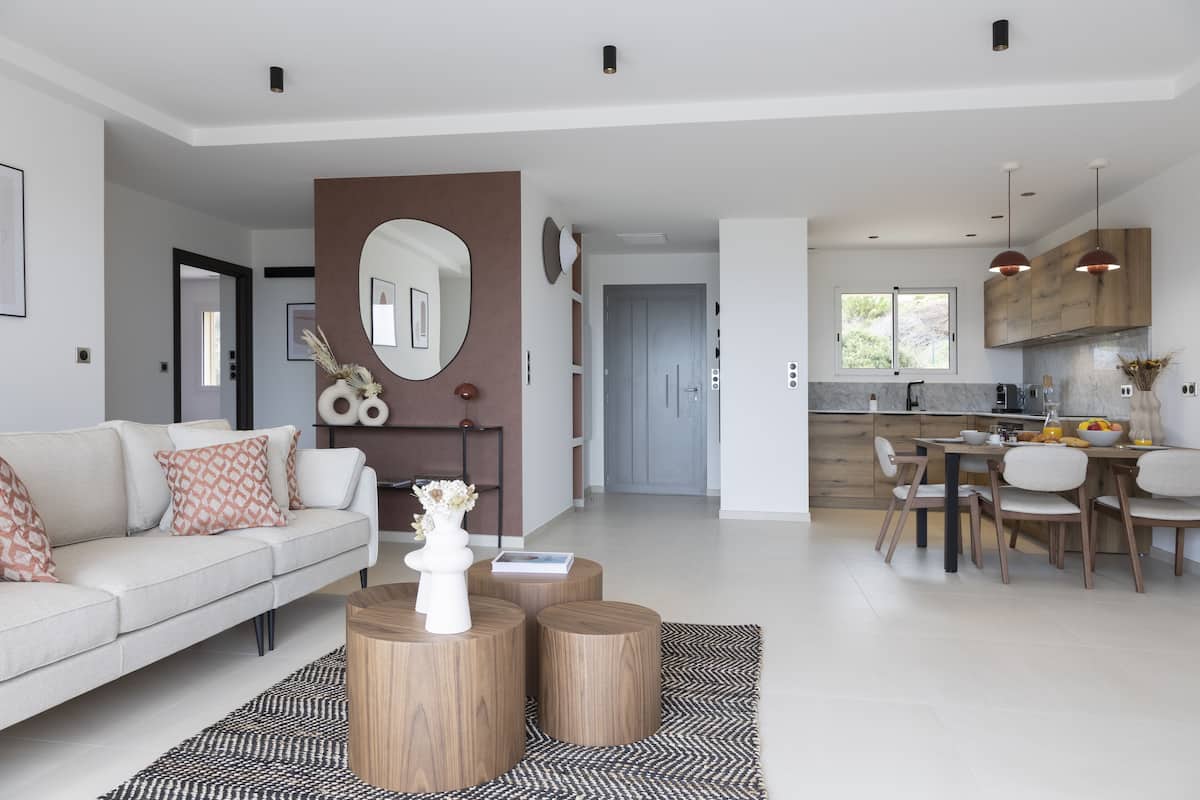 A modern living room with a sofa, coffee table, and dining area with chairs and a kitchen in the background.