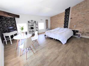 A modern bedroom with a large bed, a desk with a TV, and a dining area.