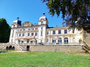 A large, historic building with two prominent domes, a stone wall, and a grassy courtyard.