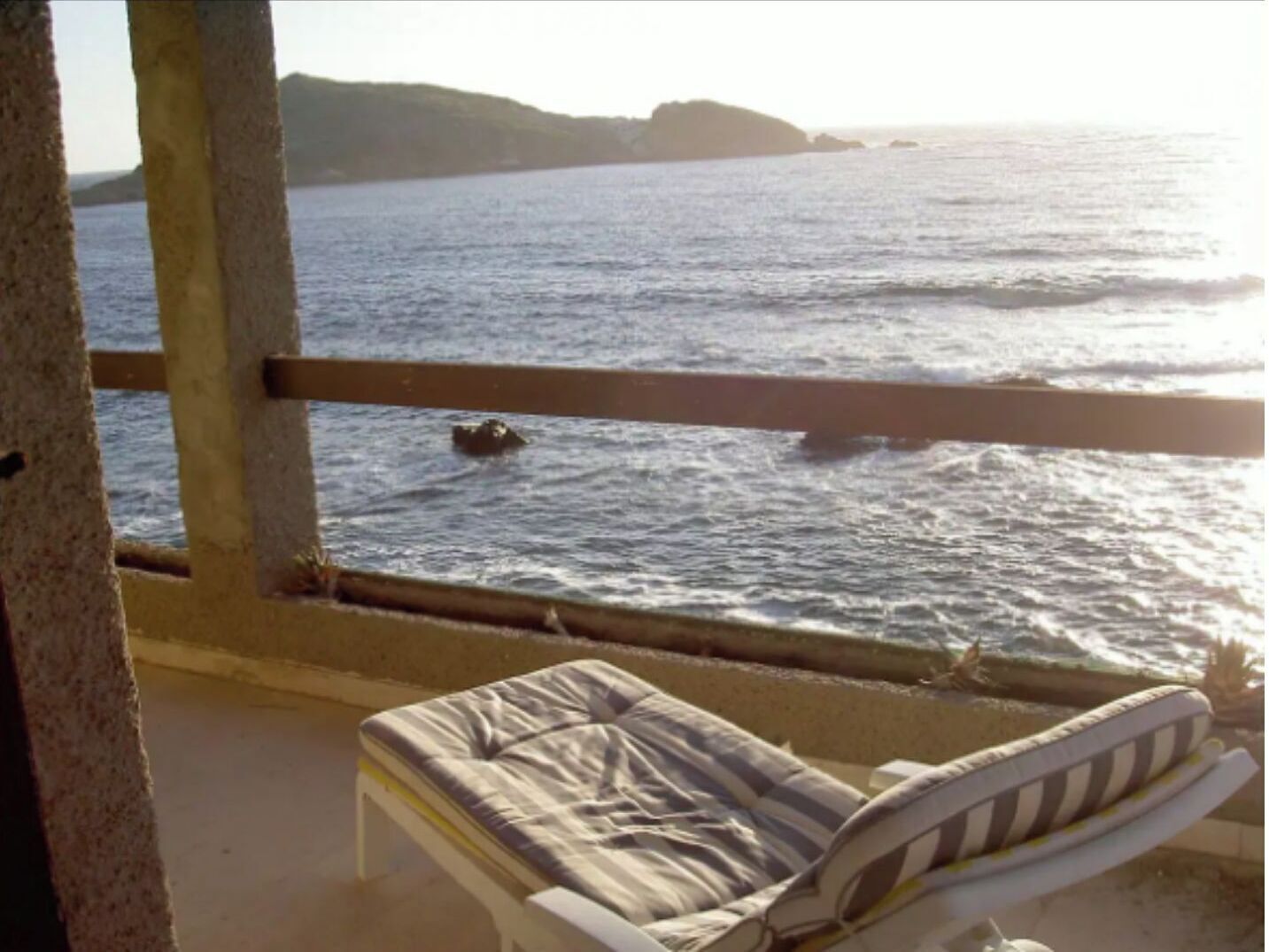 Een balkon met een enkele witte ligstoel en uitzicht op zee.