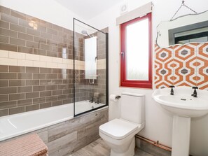Un baño con ducha envuelta en vidrio, inodoro blanco y lavamanos con un diseño llamativo en el fondo.