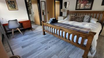 A bedroom with a wooden bed, a desk with a chair, a wardrobe, and a mirror.