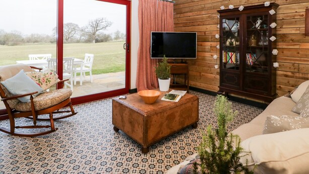 A cozy living room with a wooden interior, a sliding glass door leading to a patio, a television, and a bookshelf. - Down the Rabbit Hole (Bristol)