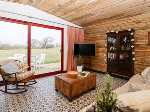 A cozy living room with a wooden interior, a sliding glass door to a patio, a television, a bookshelf, and a rocking chair.