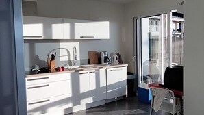 Una cocina moderna con armarios blancos, una cafetera y un lavamanos. Hay un comedor con una silla y una mesa.
