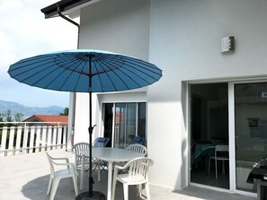 A patio with a table and chairs, a blue umbrella, and a sliding glass door leading to an indoor area.