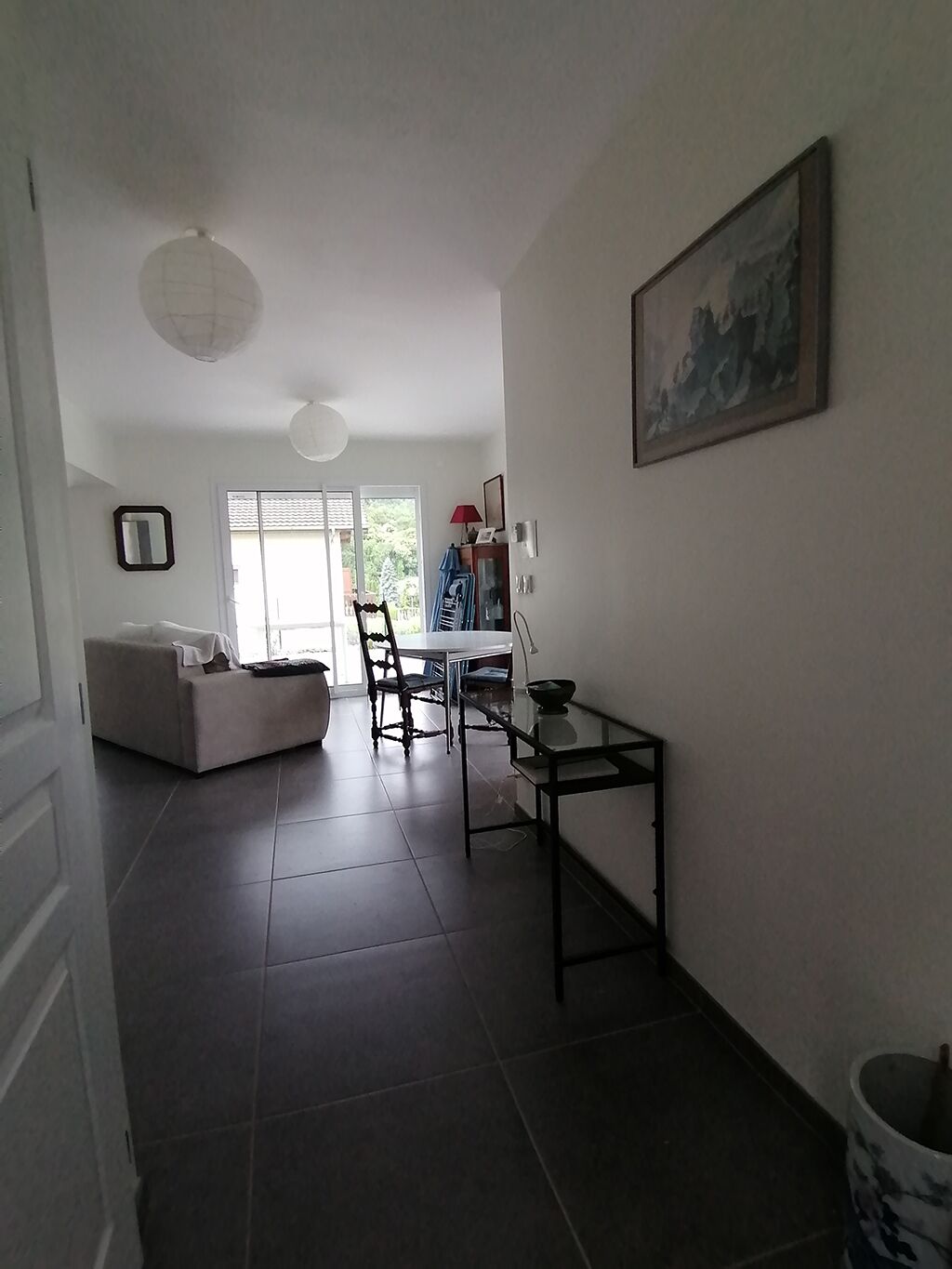 Een ruime woonkamer met een bank, eettafel en stoelen. Een groot raam zorgt voor natuurlijk licht en uitzicht op groen.