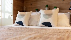 A bed with a beige carpet and white bedding, accompanied by three pillows with a geometric design. - London Gate No1 - Donnini Apartments (Kilmarnock)