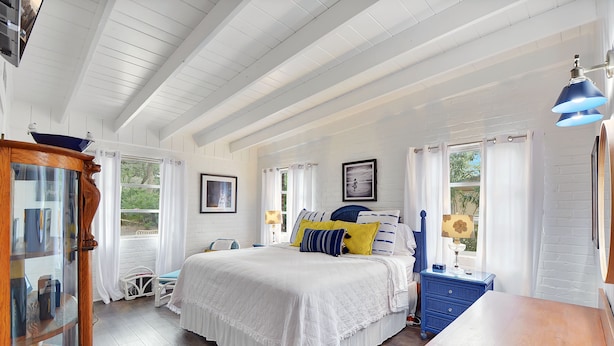A bedroom with a large bed, a dresser, a nightstand, and a window with curtains.