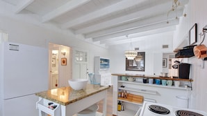 A kitchen with white cabinetry, a granite countertop, a white refrigerator, a stove, and a hanging light fixture.