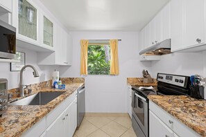 Una cocina compacta con armarios blancos, encimera de granito, ventana con cortinas amarillas y horno empotrado.