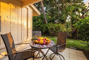 Une terrasse avec deux chaises et une table, un jardin tropical en arrière-plan et un bâtiment à l’extérieur blanc.
