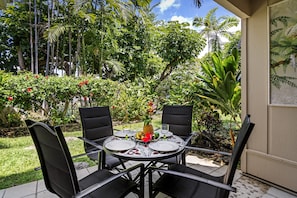A round table with four chairs, set outdoors with a tropical garden view.