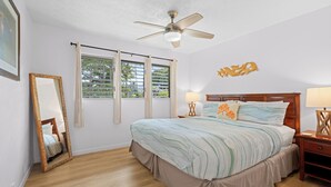 Un dormitorio con cama, mesitas de noche, ventilador de techo y ventana con persianas.