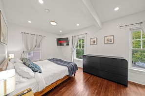 A bedroom with a bed, bedside table, lamp, curtains, a TV, and a window with a view.