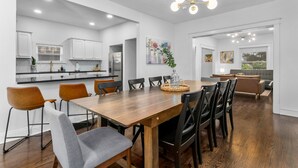 A modern kitchen with white cabinets, a wooden dining table, and a chandelier. - Midtown Getaway (Kansas City)