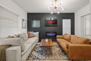 Een moderne woonkamer met een grijze bank, een bruine bank, een houten salontafel en een open haard.