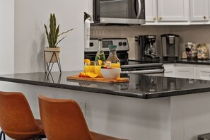 A kitchen island with a fruit bowl, a bottle of champagne, and a potted plant. - Midtown Getaway: Walk to KC Streetcar-Dining/Entertainment + Fire Pit! (Kansas City)