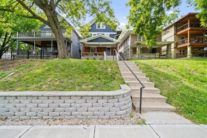 A residential area with a stone retaining wall, a set of concrete steps leading to a house, and a tree in the foreground.