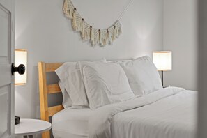 A neatly made bed with white linens, a wooden headboard, and a macrame wall hanging. - Midtown Getaway: Walk to KC Streetcar-Dining/Entertainment + Fire Pit! (Kansas City)