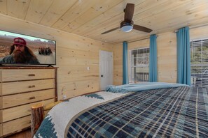 A room with a bed, a dresser, a television, and a ceiling fan.