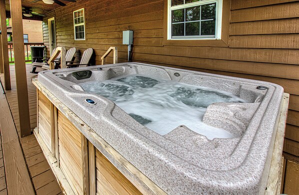 A hot tub with a stone exterior, wooden deck, and a window with blinds.