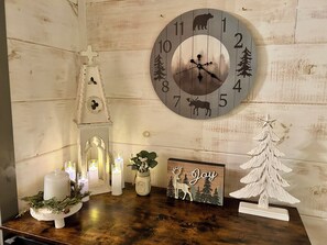 Pared de madera con un reloj, velas, un pequeño árbol de Navidad y un letrero que dice 'Joy'.