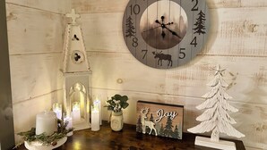 Pared de madera con un reloj, velas, un pequeño árbol de Navidad y un letrero que dice 'Joy'.