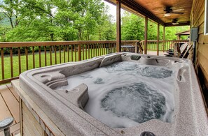 Un jacuzzi en una terraza de madera con vistas a un área verde y árboles.