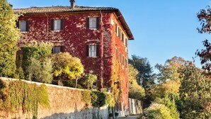 A large, multi-story building with a red facade partially covered in ivy, surrounded by trees and a stone wall. - VILLA IL PRINCIPE - Nine Bedroom Villa, Sleeps 18 (Castellina in Chianti)