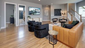 A spacious living room with a large sofa, black armchairs, and a coffee table. A television displaying "Welcome to Nashville" is mounted on the wall. - Rooftop Skyline Views DT Nash Sleeps 12 (Nashville)