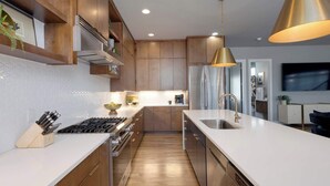 A modern kitchen with wooden cabinets, a stainless steel refrigerator, and a white countertop. - Rooftop Skyline Views DT Nash Sleeps 12 (Nashville)
