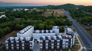 A modern apartment complex with a central courtyard, surrounded by greenery and a road. - Rooftop Skyline Views DT Nash Sleeps 12 (Nashville)