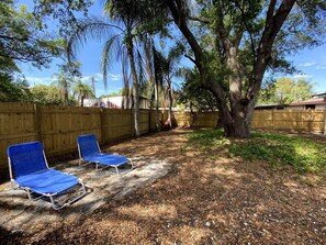 Un jardin avec deux fauteuils de jardin bleus, un hamac et une clôture en bois.
