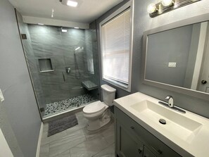 Un baño con ducha de mampara de vidrio, inodoro y lavamanos con espejo.