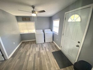 A laundry room with two washing machines, a ceiling fan, and a door with a window.