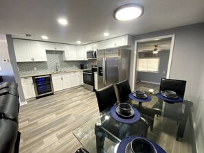 Una cocina moderna con armarios blancos, electrodomésticos de acero inoxidable y una mesa de comedor de vidrio con manteles individuales azules.