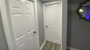 Un couloir avec deux portes blanches, un luminaire au plafond et un miroir accroché au mur.