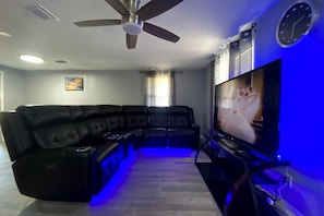A living room with a sectional sofa, a ceiling fan, a flat-screen TV, and a clock on the wall. - Spacious 3BR Sarasota Stay Near UTC & SRQ (Sarasota)