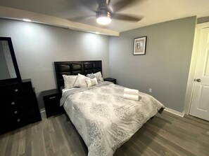 Un dormitorio con cama, mesitas de noche, cómoda, ventilador de techo y una puerta.