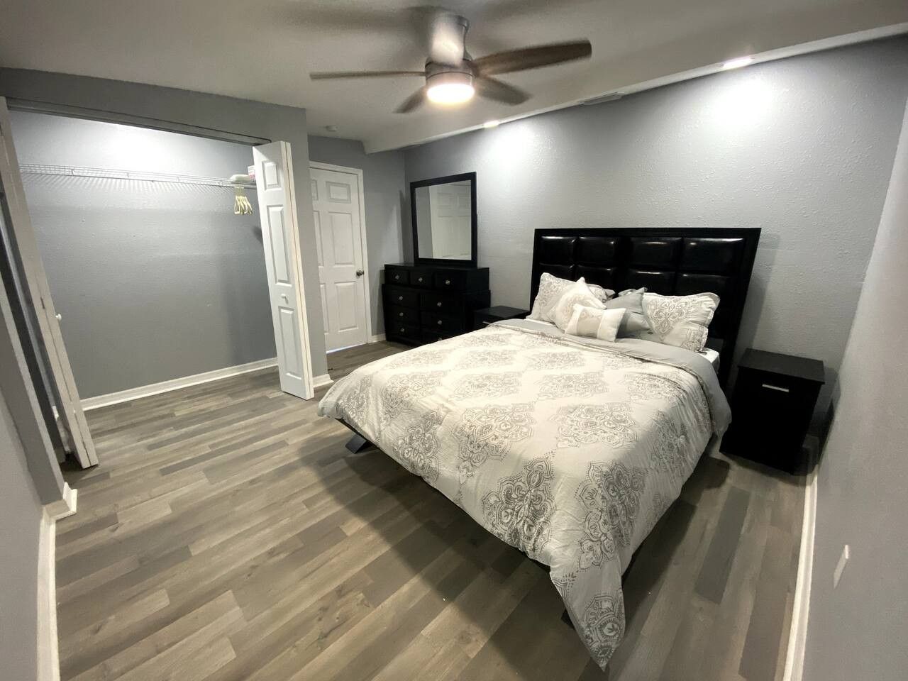 A bedroom with a bed, a ceiling fan, a dresser, and a nightstand.